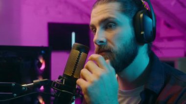 Düşünceli beyaz adam radyo spikeri mikrofon oyuncusunu tartışıyor erkek oyuncu video oyunu yayınlıyor blogger vlogger iletişim bilgisayar siber sporu pembe ışık oyunu üzerine kafa yoruyor