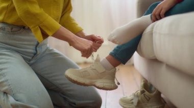Tanımlanamayan beyaz kadın anne bakıcı kadın elleri bağcıkları bağlayan bilinmeyen küçük kız çocuğu ayakkabıları bağlamaya yardım eden kız çocuğu sabah oturma odasında. Aile desteği yetiştiriliyor