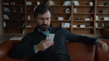 Kafkasyalı mutsuz beyaz iş adamı akıllı telefon kullanarak cep telefonuna göz gezdiriyor. Kötü haber, iflas, göz ağrısı, göz ağrısı, kapalı alanda tahriş.