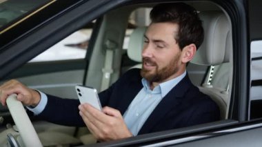 Heyecanlı Kafkasyalı iş adamı arabası cep telefonlu akıllı telefon kullanan adam başarısını kutluyor otomobil sürücüsü satın alıyor iyi haberler alıyor erkek oto kuaförünün kredi kartı zaferi hayret verici