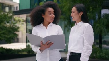 İki Afrikalı Amerikalı Asyalı kadın iş arkadaşı iş kadını çeşitli meslekdaşlar kağıt döküman dosyalarını tartışıyorlar açık havada iletişim kuruyorlar.
