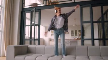Mutlu beyaz kadın, pozitif kız, evde dans eden, neşeli kız, kanepe üzerinde zıplayan, zıplayan dans eden eğlenceli hafta sonu, kablosuz kulaklıkla müzik dinleyerek eğlenceli.