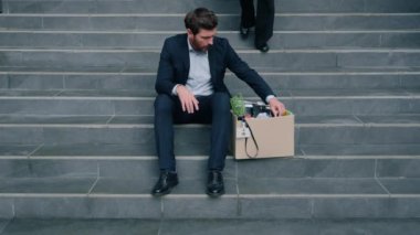 Kafkasyalı erkek, işten çıkarma kutusuyla merdivenlerde oturuyor işyerinden kovulmuş iş adamı, işsizlik krizi, kadın kız arkadaş yürüyüşü, arkadaş desteği, şehirde sakin bir konuşma.
