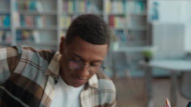 Afro-Amerikalı özgüvenli erkek öğrenci dizüstü bilgisayarı açık oturarak çalışmaya başlıyor. Sınava hazırlanıyor. İnternetten kitap okuyor, kütüphane eğitimi alıyor.