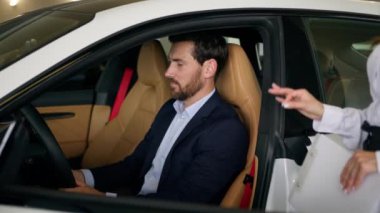 Gülümseyen orta yaşlı, beyaz erkek, erkek, işadamı, müşteri alıcısı, yeni araba kadını, kadın satış elemanı, galeride danışmanlık yapmak için araba kiralama servisini seçiyor.