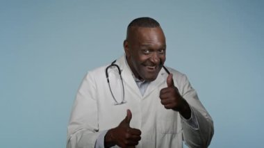 Mutlu Afro-Amerikan erkek doktor stüdyo mavi arka planda, erkek müşteri sağlığı çalışanı onaylı, onaylı sağlık hizmeti önerisi gösteriyor.