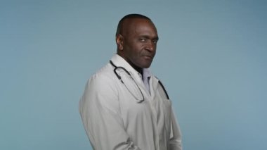 Başarılı özgüvenli Afrikalı Amerikalı adam profesyonel sağlık uzmanı erkek doktor doktor doktor cerrah kardiyolog doktor doktor doktor doktor sağlık görevlisi mavi arka planda poz veren kameraman