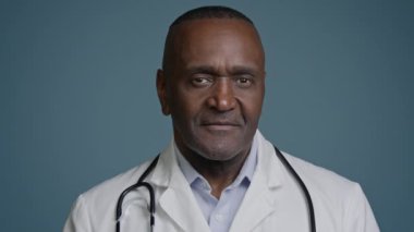 Portre erkek özgüveni olan başarılı Afro-Amerikan Etnik doktor, profesyonel sağlık çalışanı. Stüdyo mavi arka plan hastane klinik hizmetlerinde gülümseyen kameraya bakıyor.