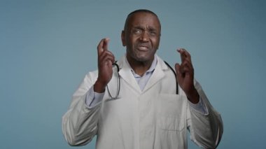 Umut dolu Afro-Amerikan erkek doktor erkek doktor erkek sağlık çalışanı şans diliyor stüdyo mavi arka planda dilek diliyor zafere inanmaya yardım edin büyük bir sonuç bekleyerek dua edin rüya görün