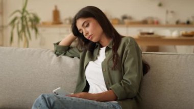 Sıkıcı üzgün üzgün sinirli Arap kadın stresli Hintli bayan İspanyol bayan üzgün üzgün cep telefonlu akıllı telefonlu istenmeyen hamilelik sorununu evdeki koltukta düşünmekten yorgun düşmüş.