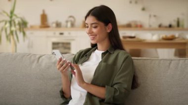 Mutlu gülümseyen Arap kadın Hintli kadın İspanyol kadın cep telefonu bağımlısı uygulama web akıllı telefonu kullanıyor sosyal medya cep telefonu sohbeti ev içi internet alışverişi