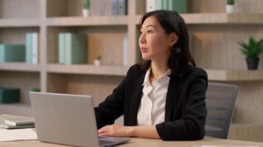 Düşünceli iş kadını Asyalı yetişkin iş adamı kadın yönetici Çinli Koreli kız Japon işveren kadın girişimci internetten kameraya bakıp mutlu bir şekilde gülümsediğini düşünüyor.
