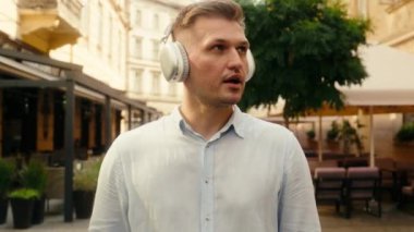 Kafkas erkek işadamı iş adamı mutlu turist gezgini dışarıda gezgin neşeli, güler yüzlü erkek sokakta yürüyen kulaklıkla müzik dinliyor git ve kulaklıkla şehirde şarkı söyleyen kulaklıkları dinle.