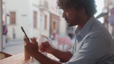 Şehirdeki Hintli adam cep telefonu sosyal medya kullanarak kahve içiyor. Erkek turist bilet ayırtıyor. İnternetten alışveriş yapıyor.