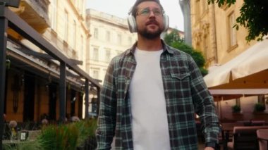 Kafkasyalı mutlu erkek işadamı turist gezgini yaz tatilinde dışarıda kaygısız adam kulaklıkla müzik dinliyor sokakta yürüyor ses kulaklıkları dinliyor telefonda şarkı söylüyor şehirde