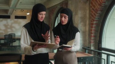 İki Müslüman İslami iş kadını tesettüre girmiş Arap kızlar bayan iş arkadaşları iş ortakları mimar dijital tablet kullanıyor proje asistanı ofiste kadın çalışmaları yazıyor
