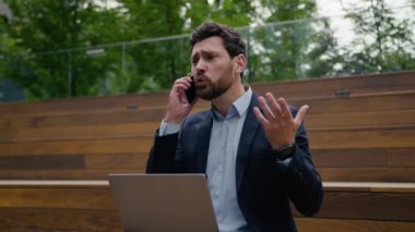Sinirli, kızgın, Kafkas işadamı öfkeli iş adamı uzak bir laptopta çalışıyor erkek adam dışarıda konuşuyor cep telefonuyla konuşuyor kavga ediyor kavga çığlıkları atıyor cep telefonunu atıyor.