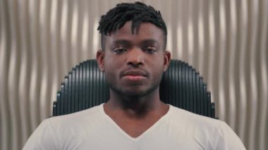 Sakin olun, yorgun, yorgun, Afro-Amerikan, erkek, erkek, oyun programcısı, modern, fütürist, beyaz oda, kapalı siber uzay, kapalı gözlerde dinleniyor, kameranın yüzüne bakıyor.