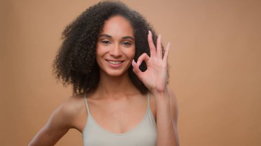 Afro-Amerikan model güzel çekici bir kız bej stüdyo arka plan güzellik prosedürü kameraya gülümsüyor tamam kabul et kozmetik reklamı sağlık cilt bakımı