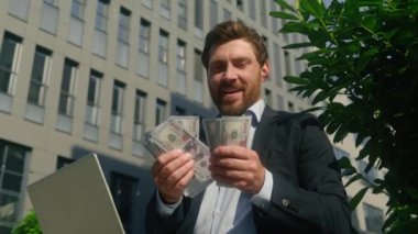 Mutlu gülümseyen Kafkasyalı zengin orta yaşlı işadamı işadamı işadamı işveren erkek yatırımcı dolar sayıyor şehirde para sayıyor maaş borsa kârı dizüstü bilgisayarlı kumarhane.