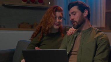 Gülümseyen Kafkasyalı aile evli karı koca internetten alışveriş yapan kadın internetten mal seçiyor akşam evde dizüstü bilgisayarla sipariş teslimatını tartışıyorlar.