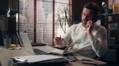 Kafkasyalı orta yaşlı bir adam cep telefonuyla konuşuyor ofis işlerinde çoklu iş görüşmesi erkek şirket patronu iş adamı tüccarlarına bilgisayar kağıtlarıyla yürütme planları yapıyor.