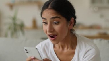 Mutlu gülümseme heyecanlı sevinç şaşkın şaşırmış Hintli Hintli kadın Arap kadın evde harika haberler okuyor internet üzerinden internet başarısı teklif ediyor cep telefonu zaferi kazanıyor akıllı telefon kazanıyor