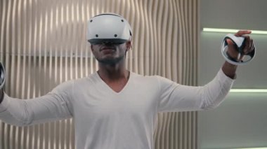 Fütürizm konsepti modern eğlence video oyunu sanal gerçeklik VR gözlüklü erkek oyuncu içeride beyaz fütüristik odada oyun oynuyor metaevren rahatlığı