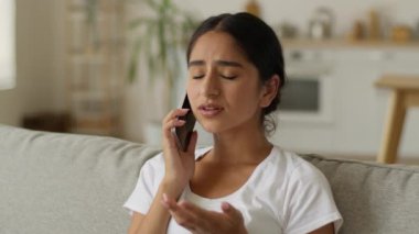 Sorun akıllı telefon konuşması üzgün Hintli kadın hayal kırıklığına uğramış Hintli kız Arap kadın ev konuşması cep telefonu kanepe dairesinde hayal kırıklığına uğramış kötü haber iletişimi.