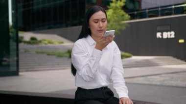 Sinirli Asyalı Koreli kadın iş kadını ses kaydı. Elinde cep telefonu, akıllı telefon görüşmesi var. Şehir merkezinin dışında.