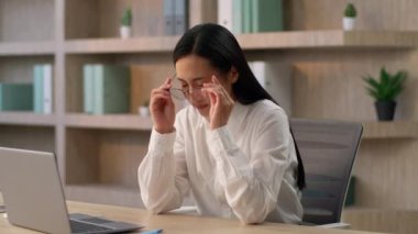 Gergin Asyalı iş kadını kadın Çinli iş kadını ofis bilgisayarında çalışan iş kadını gözlüklerinizi çıkarın gözlerinizi ovuşturun gözlerinizi acıdan uzak tutun gözlerinizi yorun.