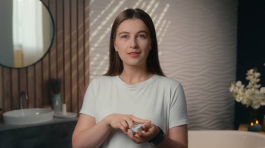 Beyaz, gülümseyen kadın kadın güzellik ürünlerini cilt bakım kremi nemlendirici vücut losyonu doğal kozmetik hidrat güneş kremi nemlendirici yumuşak cilt bakım evi banyosuna sürüyor.