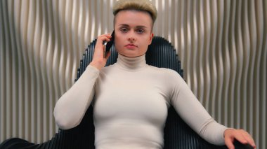Kafkasyalı kadın oyuncu kullanıcı programcısı kadın hacker iş kadını siyah koltukta oturuyor fütürist stüdyo siber güvenlik modern yenilik cep telefonu kendine güvenen iş kadını kameraya bakıyor