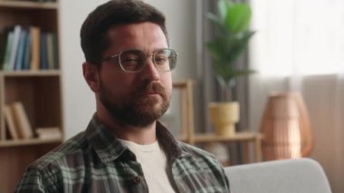Evdeki portre sakallı adam ev sahibi ev sahibi ev kredisi kredi sigortası koltukta oturup kameraya bakıyor gözlük takıp sağlık sigortası yaptırıyor.