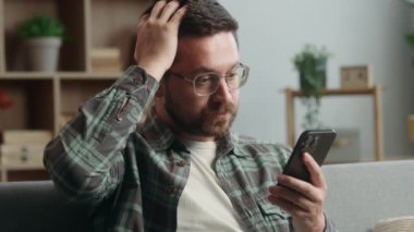 Kafkasyalı erkek kullanıcı cep telefonu uygulamasına göz atıyor sosyal medya akıllı telefon şoku kötü haber sorunu şaşırttı şaşırttı şaşırttı şaşırttı internet sitesi ev kanepede kanepe
