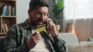 Stresli, sinirli, sinirli, Kafkasyalı erkek, online alışveriş yapıyor, çağrı desteği konuşuyor, banka konuşmalarına yardım ediyor, cep telefonu, akıllı telefon, evde kredi kartını bloke ediyor.