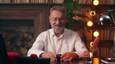 Kafkasyalı mutlu bir Avrupalı adam elinde kek tutarak yanan mumu üflüyor. Mutlu bir doğum günü tatili diliyorum. Yaşlanan yaşlı, emekli işadamı iş hayatını ofis içinde kutluyor.