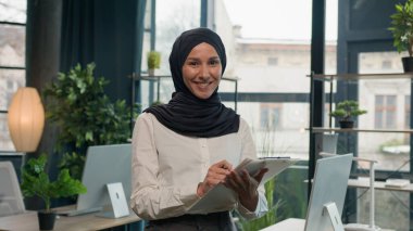 Mutlu Müslüman Müslüman kadın tesettürlü Arap kız, kağıt tabletle İK müdürü, notlar yaz, not tableti imzala, yapılacaklar listesi iş görüşleri başarılı iş kadını iş akışı planlama