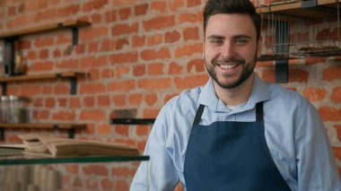 Kafkasyalı gülümseyen beyaz erkek garson profesyonel barmen kafeteryada tezgahın arkasında kahve yapıyor restoranda müşterilere servis yapıyor mutlu erkek kafe çalışanı küçük işletme sahibi kameraya bakıyor