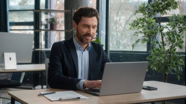 Caucasian businessman typing on laptop checking email standing in office morning in sunbeams sunrise man successful entrepreneur professional manager leader corporate executive smiling looking camera