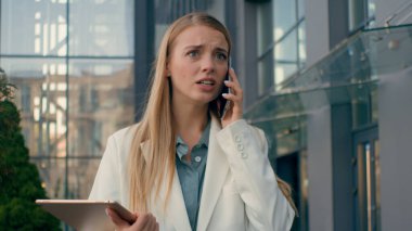 Sinirli, sinirli, stresli, beyaz kadın iş kadını ofis yakınında yürüyor ve cep telefonu müdürü bayan girişimci hakkında konuşuyor. Hoş olmayan bir iş görüşmesine akıllı telefon kullanarak cevap veriyor.
