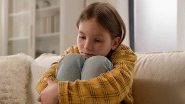 Frustrated depressed little Caucasian child girl preteen daughter hug legs punished bad behavior. Sad schoolgirl kid thinking domestic problems school family abuse stress custody adoption home couch clipart