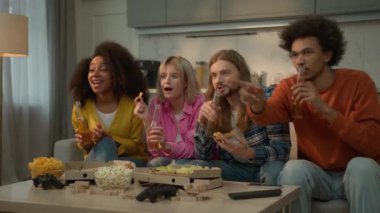 Dört farklı etnik çeşitlilikte arkadaş, beyaz kadın, Afrikalı kadın erkek, erkek, televizyon izlemekten zevk alıyor, kanepede pizza yiyor, hafta sonu arkadaşlığı yiyor.