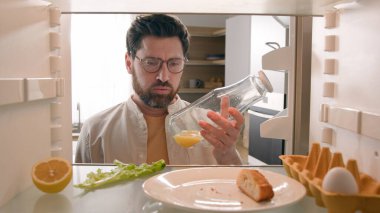 Man open empty refrigerator with half lemon lettuce leaf one egg slice of bread leftover orange juice in bottle find solution order food delivery with mobile phone app point of view from inside fridge