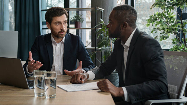 Caucasian lawyer show online offer to African American client man bank insurance consultant consult client about contract document. Two multiracial men businessmen in office discuss laptop project