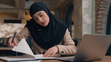 Kadın tesettürlü Müslüman kadın ofis müdürü iş kadını, Kafe 'de dizüstü bilgisayarla çalışan Arap İslamcı kız serbest çalışan öğrenci müşteri telefonuna danışmanlık yapıyor.