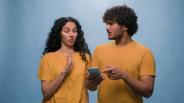 İnternet üzerinden cep telefonu alışverişi yapan çok ırklı bir çift, kadın ve erkek bilet seçiyor, teslimat siparişi veriyor, mavi stüdyo arka planında birleşik aile bütçesini onaylıyor.