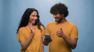 İnternet üzerinden cep telefonu alışverişi yapan çok ırklı bir çift, kadın ve erkek bilet seçiyor, teslimat siparişi veriyor, mavi stüdyo arka planında birleşik aile bütçesini onaylıyor.