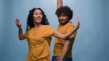 Çok ırklı çift, Hintli Arap erkek İspanyol, beyaz kadın, müzik eşliğinde dans ediyor. Eğlenceli, hareketli dans ediyor. Mavi arka planda eğleniyor.