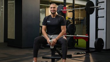 Yorgun Afrikalı Amerikalı sporcu spor salonundaki spor salonundaki spor şişesinden protein takviyesi içen adam yorgun sporcu erkek vücut geliştirme çalışmalarından sonra ferahlatıcı bir içecek içti.